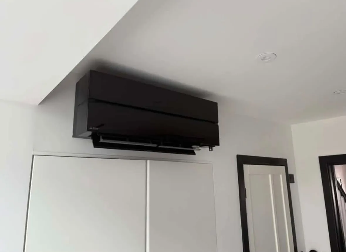 Black wall-mounted air conditioning unit fitted above built-in cupboards