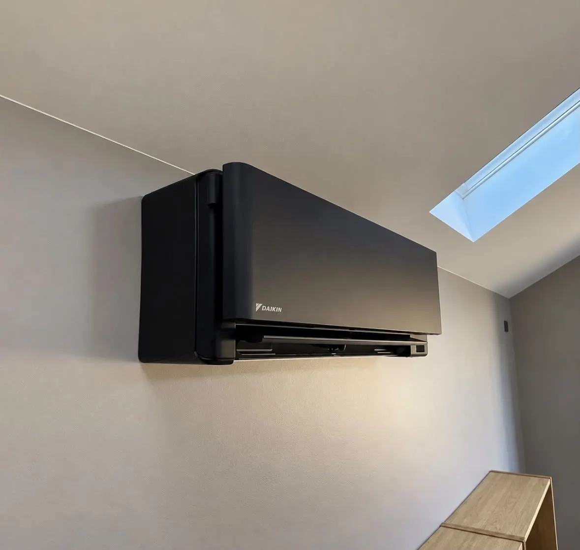 Black wall-mounted air conditioning unit in a room with a roof light