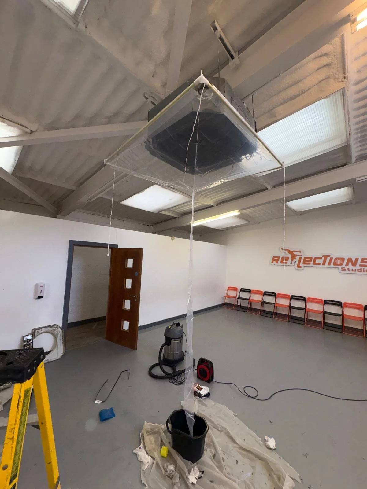 Ceiling cassette air conditioning unit being deep cleaned, with a cleaning cover fitted and draining into a bucket