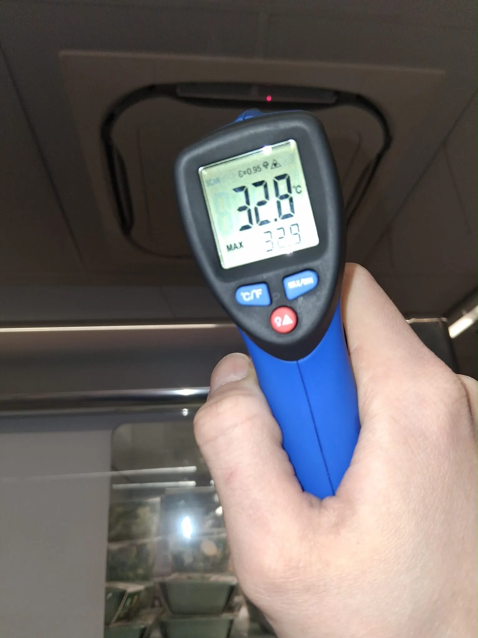 Infrared thermometer held up to a ceiling cassette air conditioning unit, showing a temperature reading