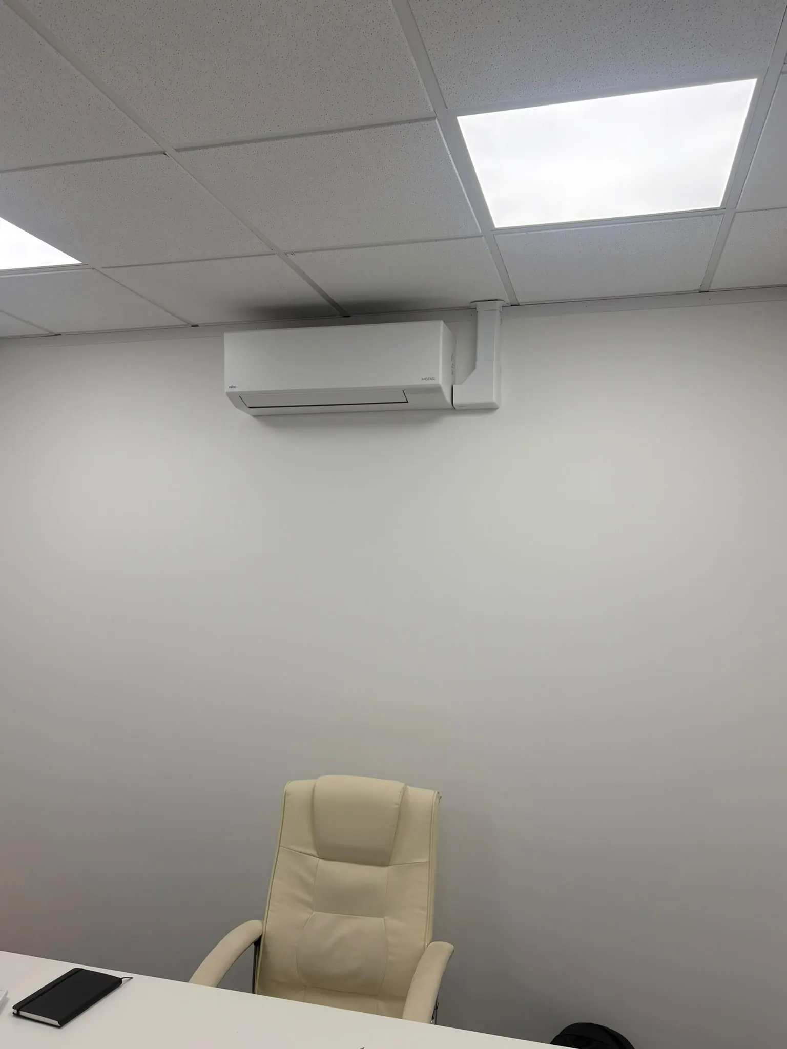 Wall-mounted air conditioning unit on an office wall above a desk and chair