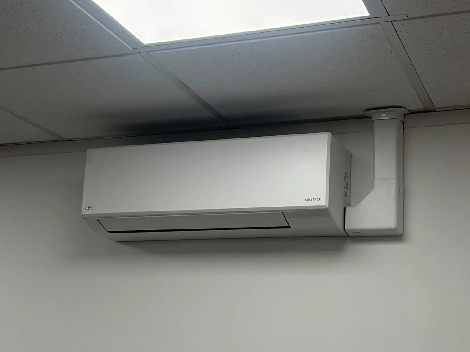 Wall-mounted air conditioning unit fitted below a suspended ceiling in an office