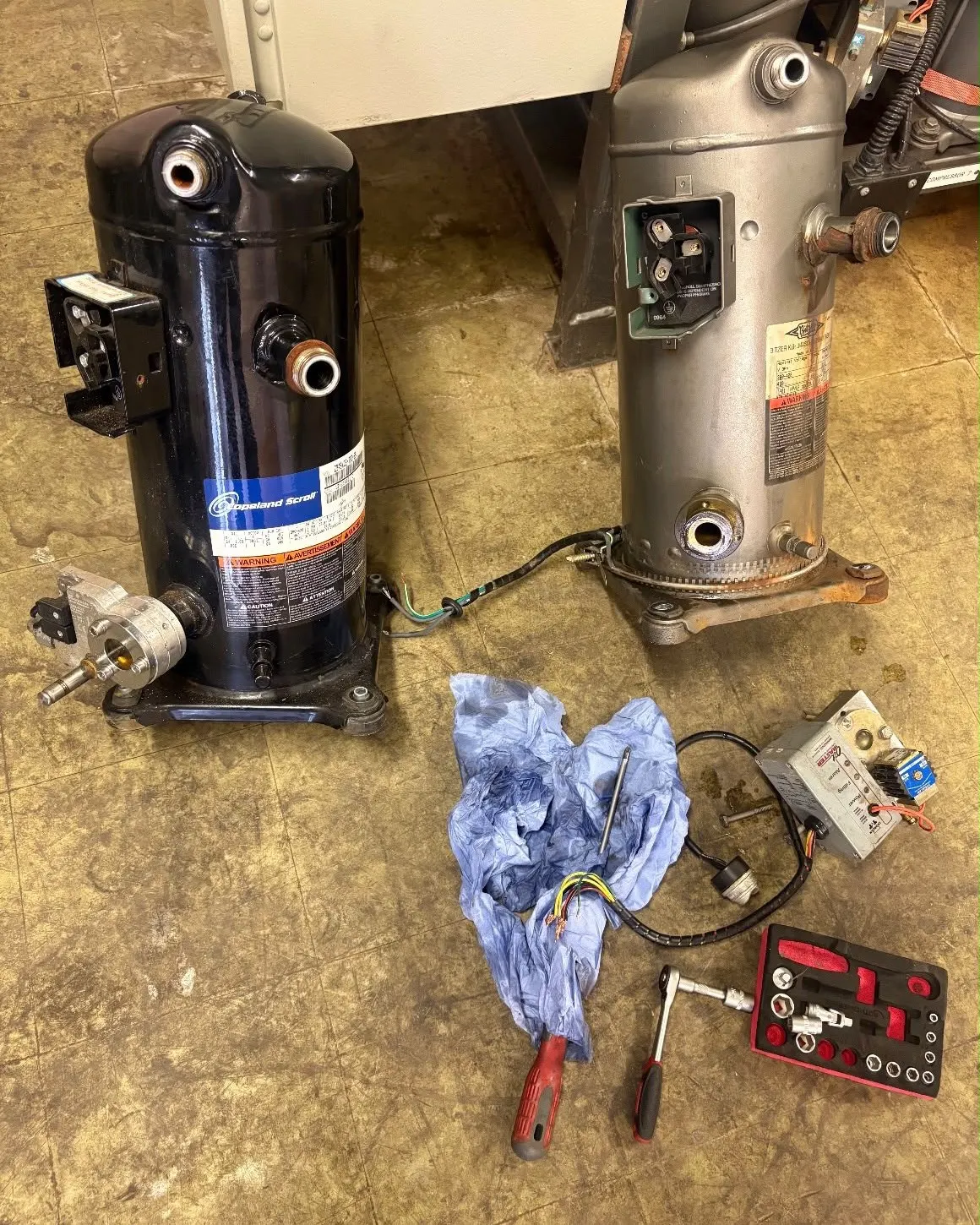New and old scroll compressors side by side on the floor during a repair