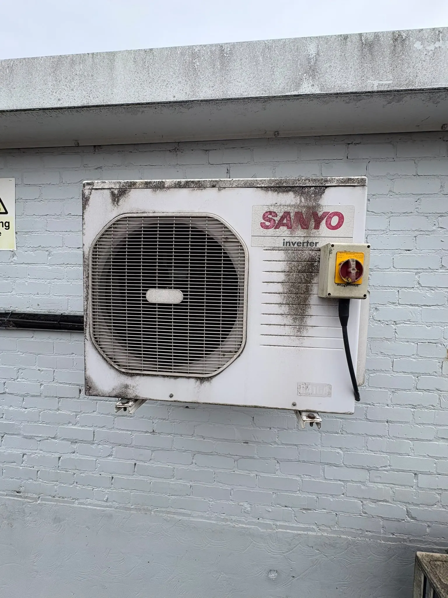 Wall-mounted outdoor air conditioning unit marked with dirt and grime before cleaning