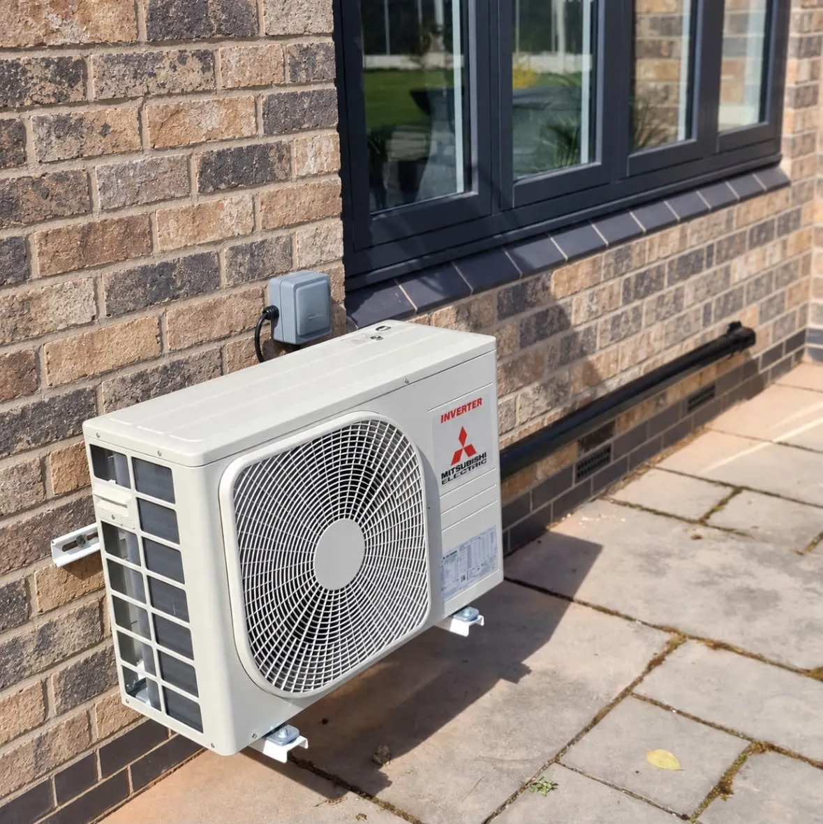 Outdoor air conditioning unit on wall brackets below a window on a brick house
