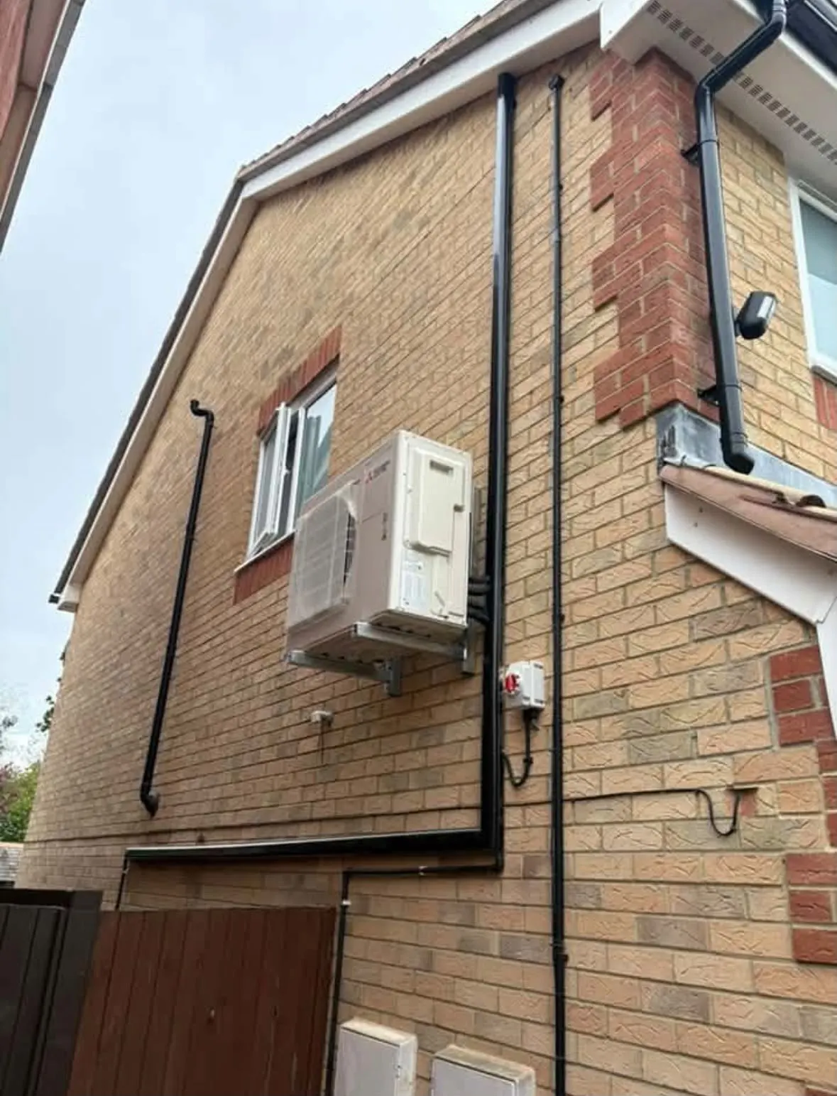 Outdoor air conditioning unit on wall brackets on the gable wall of a house, with black pipe covers