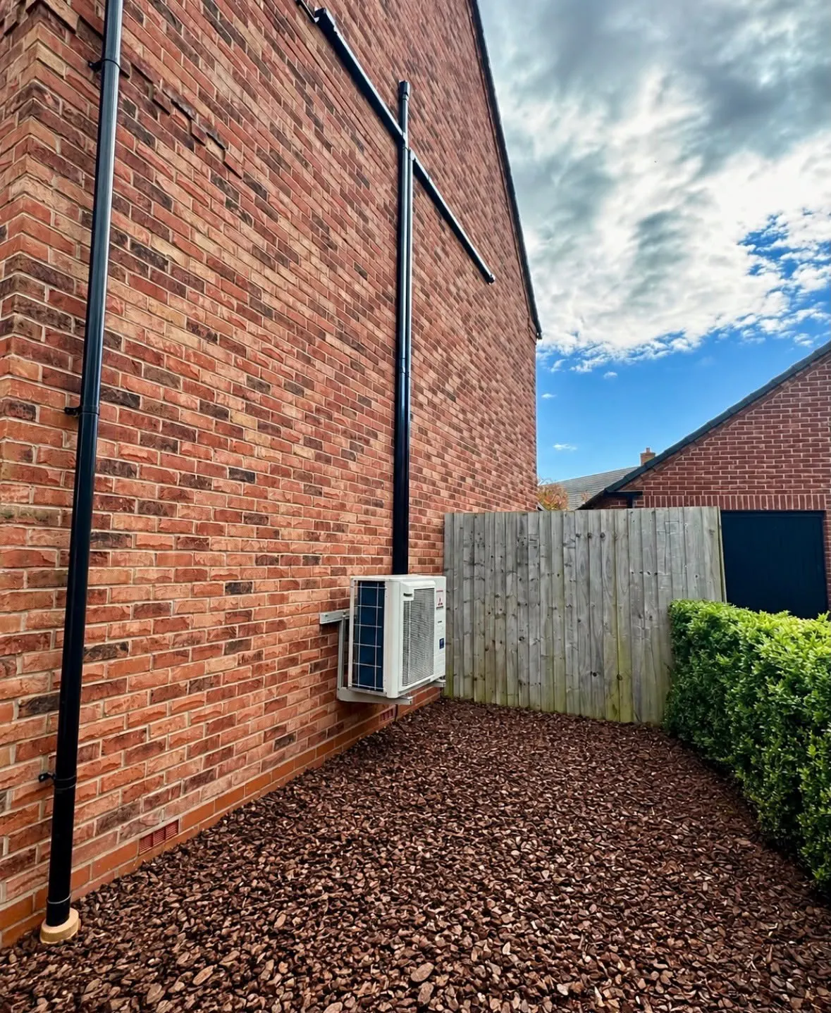 Outdoor air conditioning unit on wall brackets at the side of a brick house