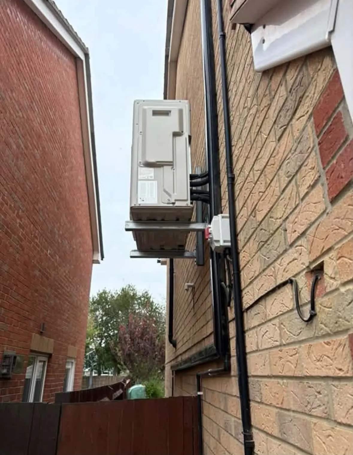 Outdoor air conditioning unit mounted on wall brackets on the side of a house