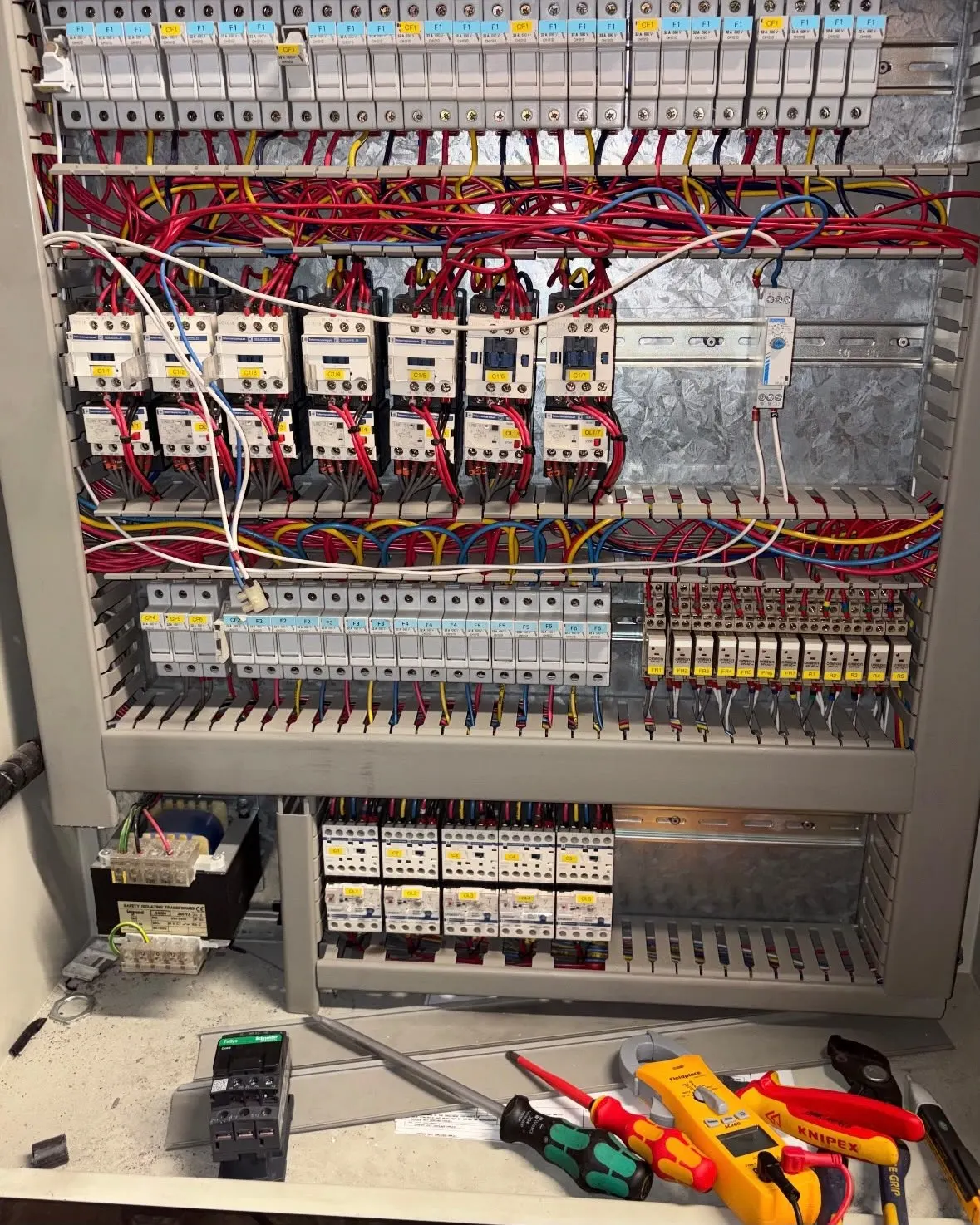 Refrigeration control panel with contactors and wiring, with a clamp meter and hand tools below