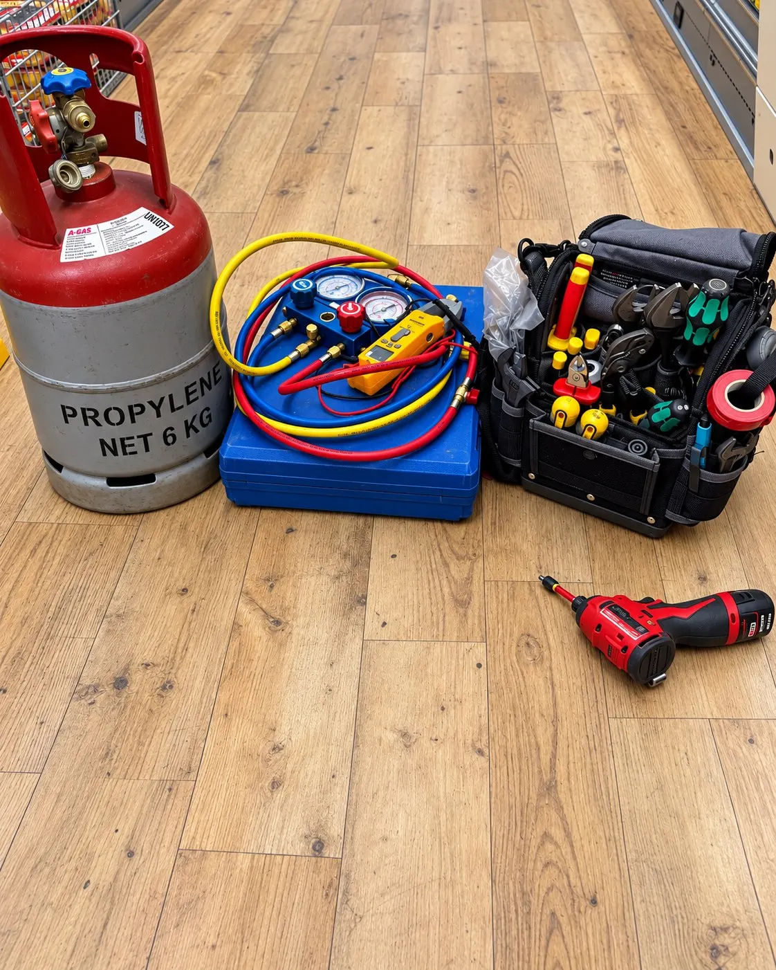 Gas cylinder, manifold gauges, clamp meter and tool bag set out on a shop floor
