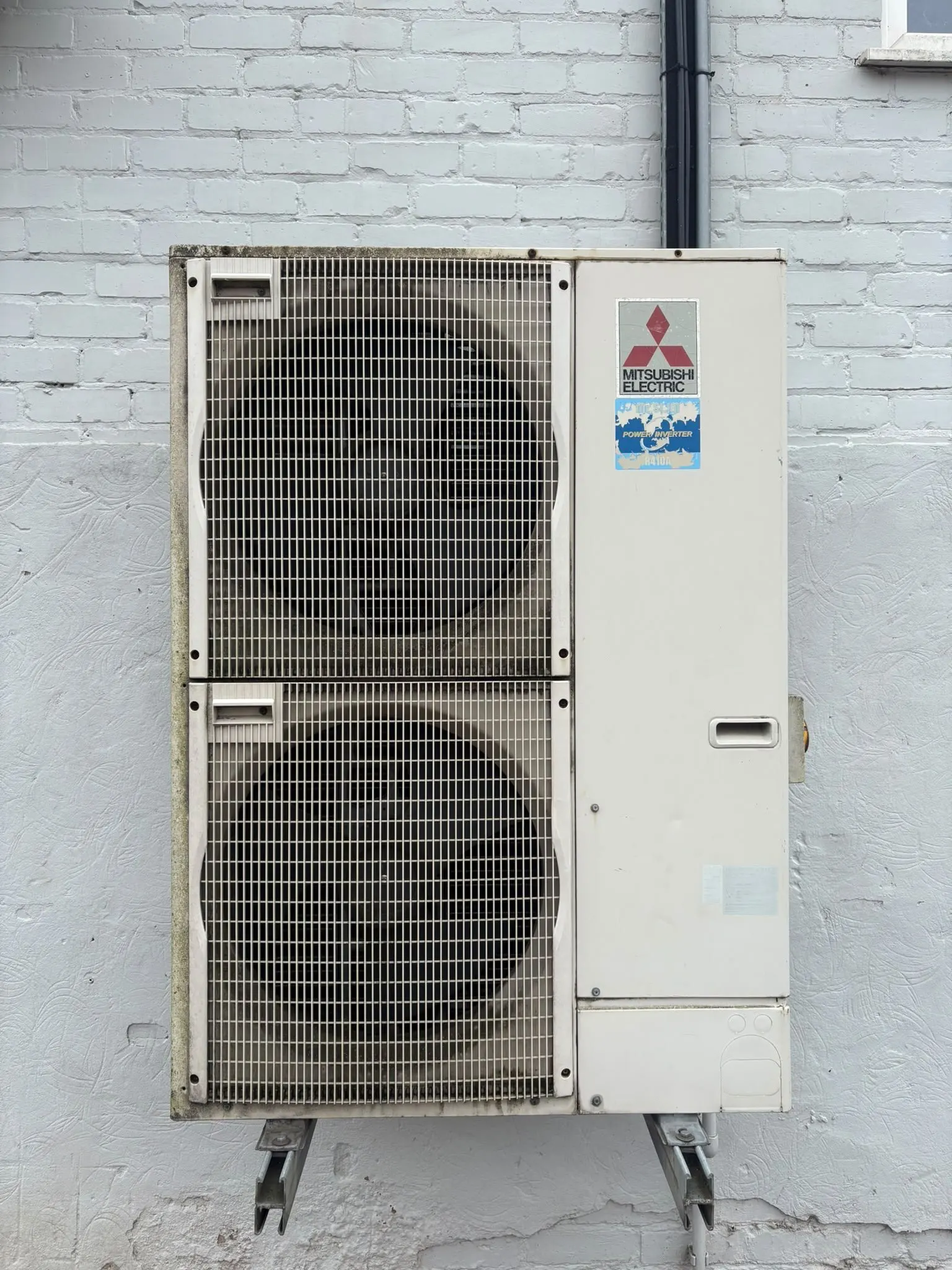 Twin-fan outdoor air conditioning unit with dirt and green staining before cleaning