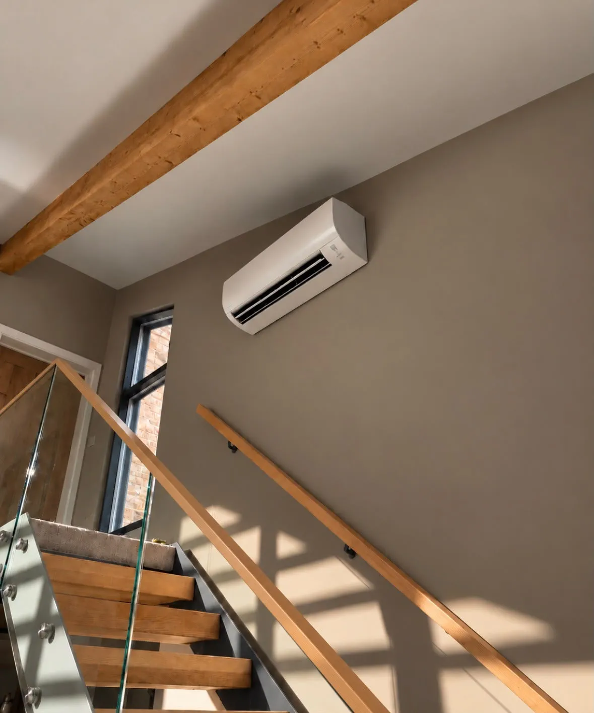 Wall-mounted air conditioning unit on the wall above a timber staircase with a glass balustrade