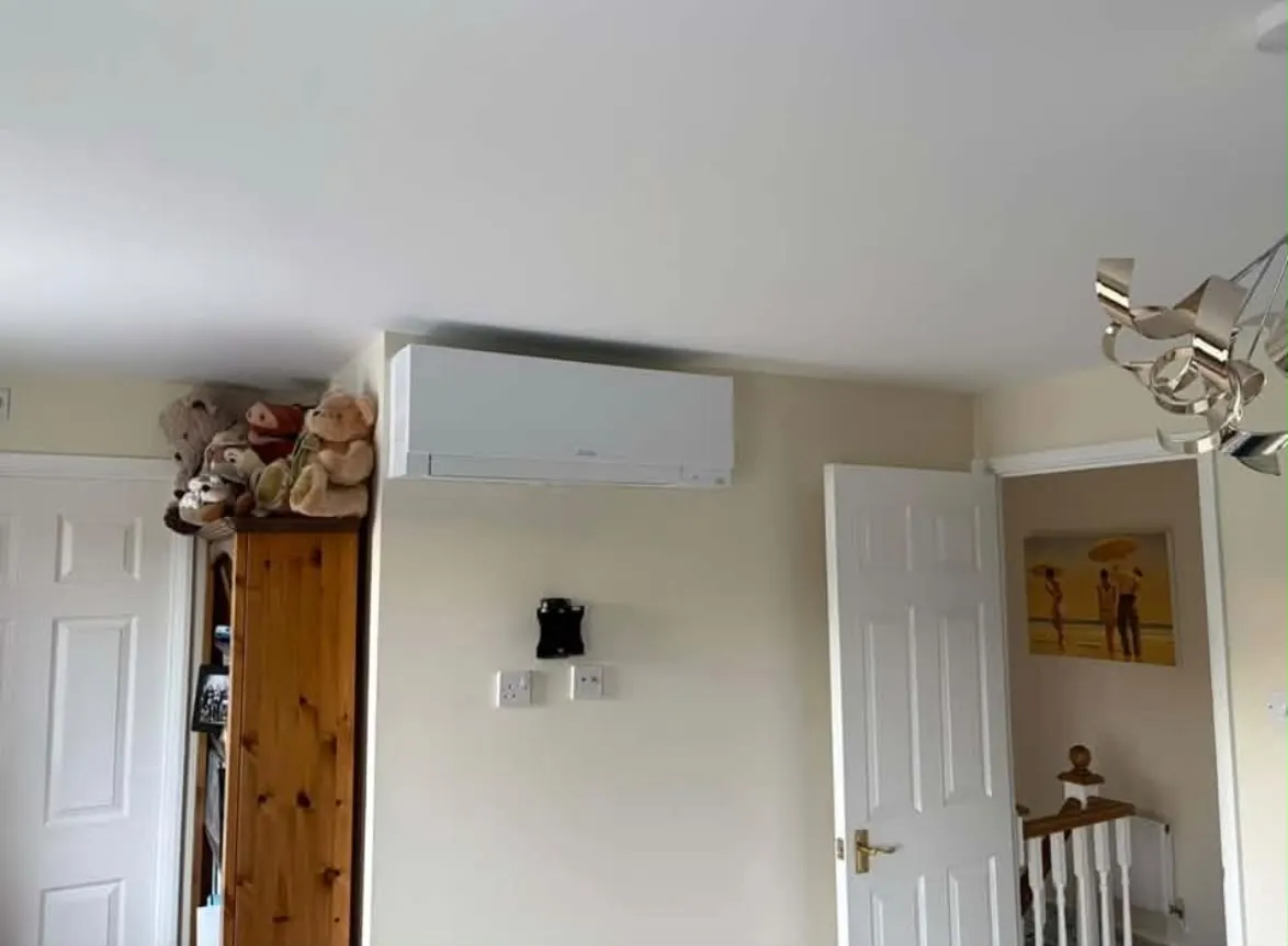 White wall-mounted air conditioning unit fitted high on the wall of an upstairs room