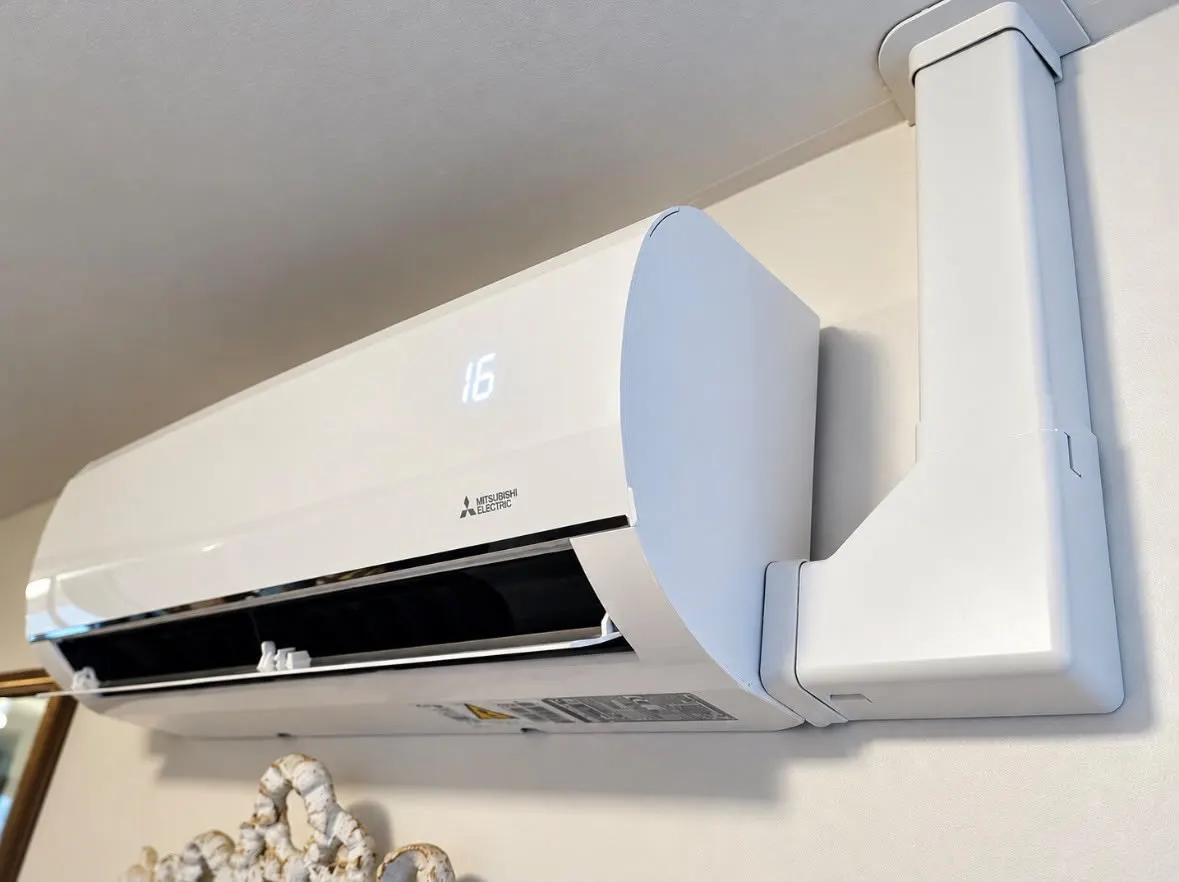 Close-up of a white wall-mounted air conditioning unit with white pipe trunking
