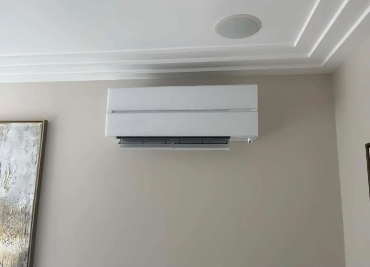 White wall-mounted air conditioning unit on a painted wall beside a framed picture